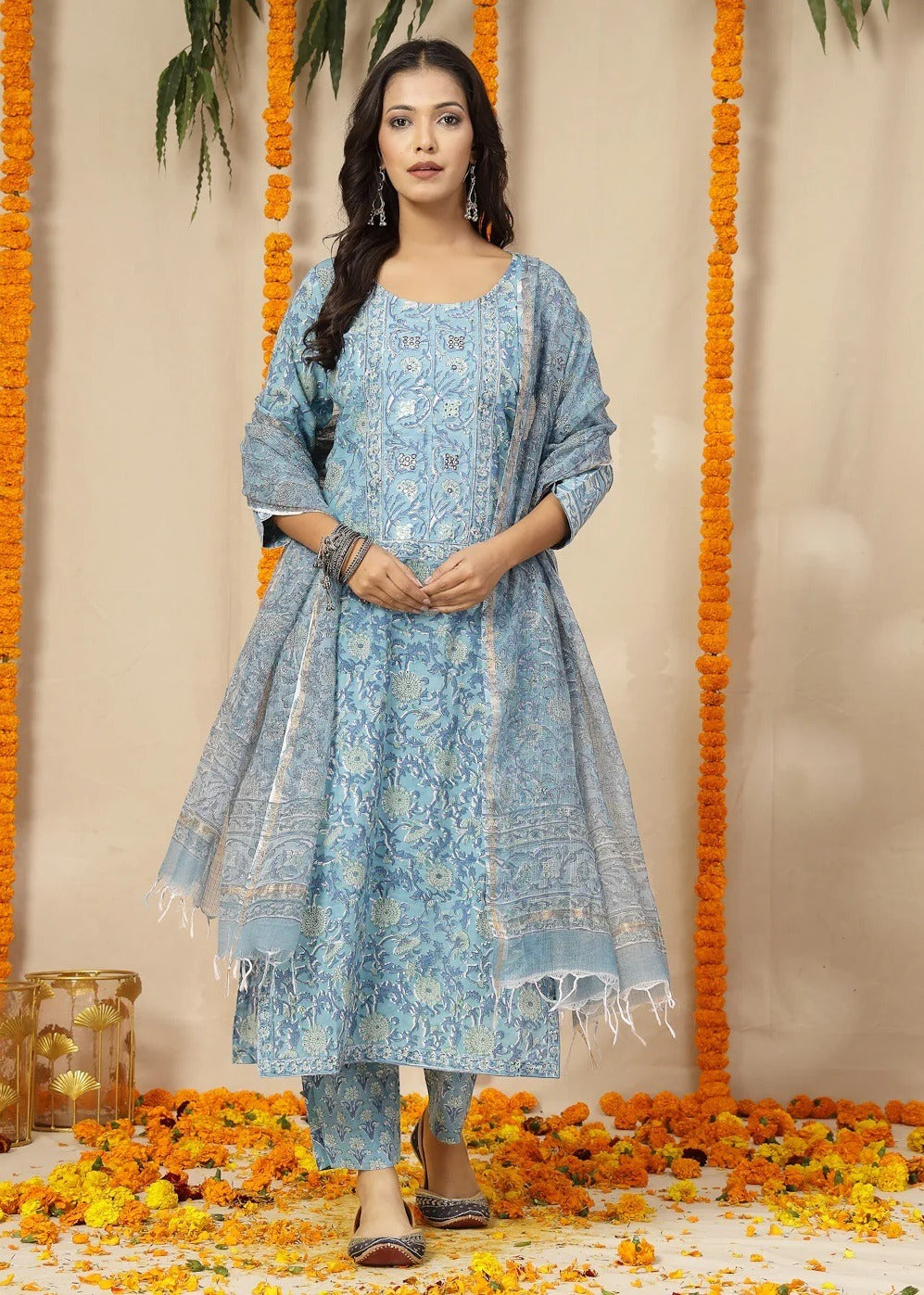 Woman in a blue traditional outfit standing in front of floral decorations.