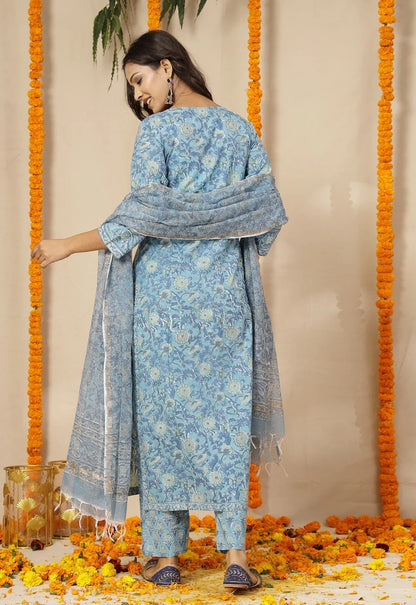 Woman in a blue floral traditional outfit standing against a decorated background with marigold flowers.