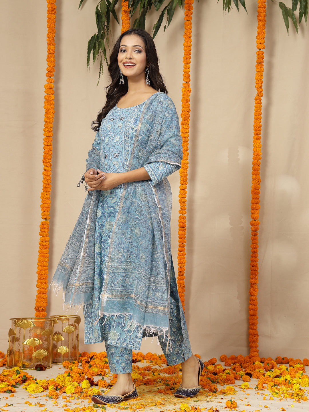 Woman in a blue traditional outfit standing on a decorated swing with flowers.