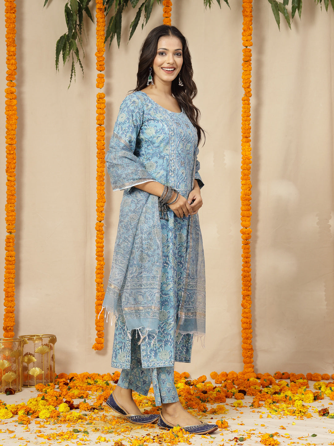 Woman in a blue traditional outfit standing in front of decorative orange marigold flowers.