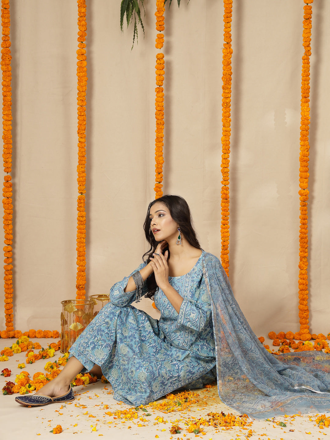 Woman in a blue traditional outfit sitting on the ground with floral decorations around her.